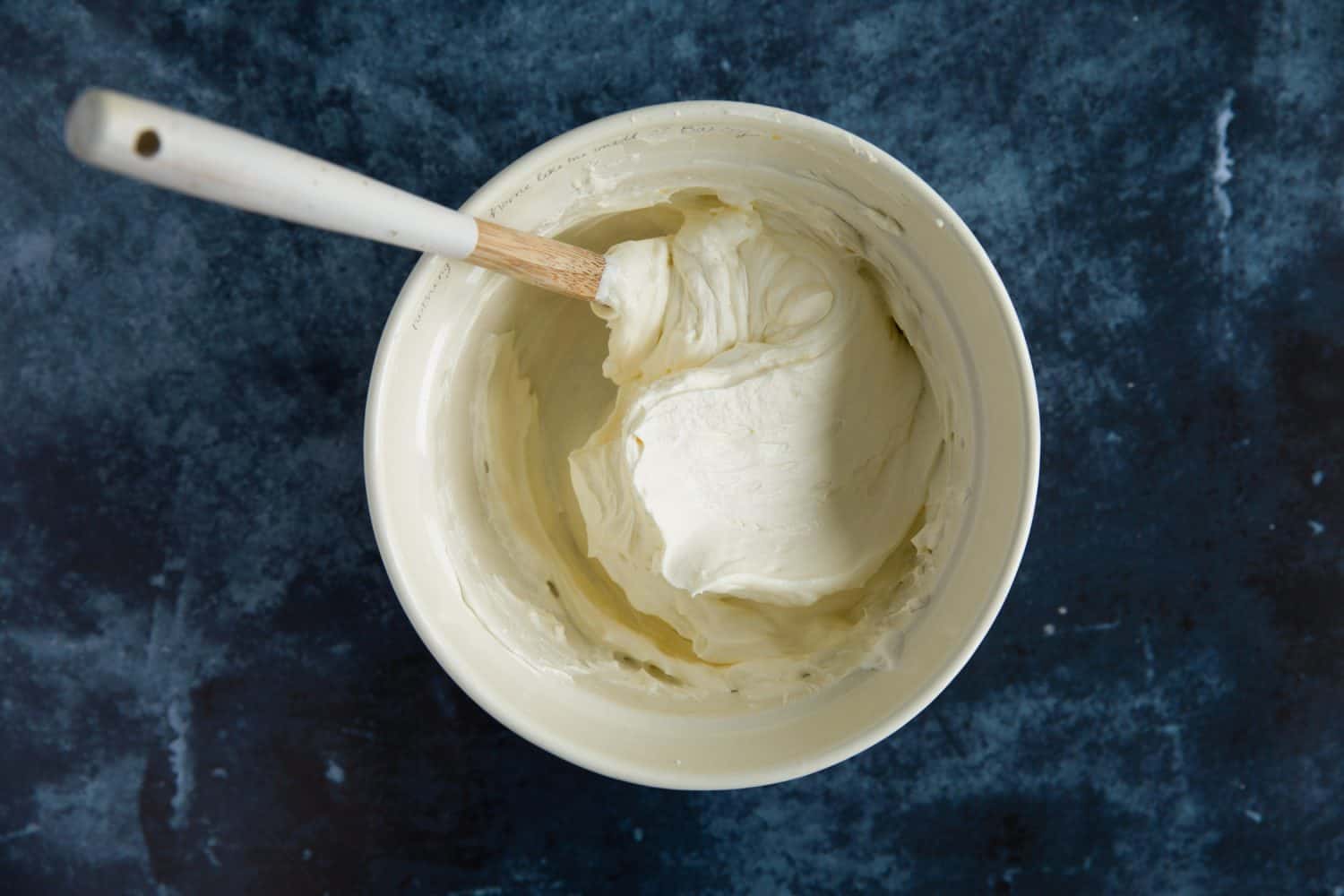 A white ceramic mixing bowl with cream cheese and whipped cream mixture. 