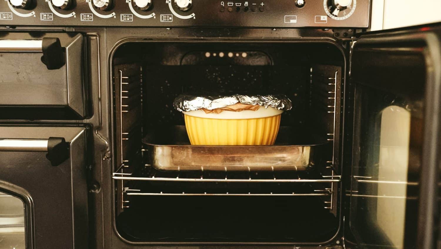 An oven with the door open and a roasting tin and pudding bowl on the oven shelf. 