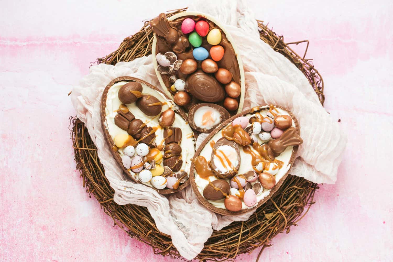 An Easter nest with 3 halves of chocolate Easter eggs on top filled with dessert and creme eggs. 