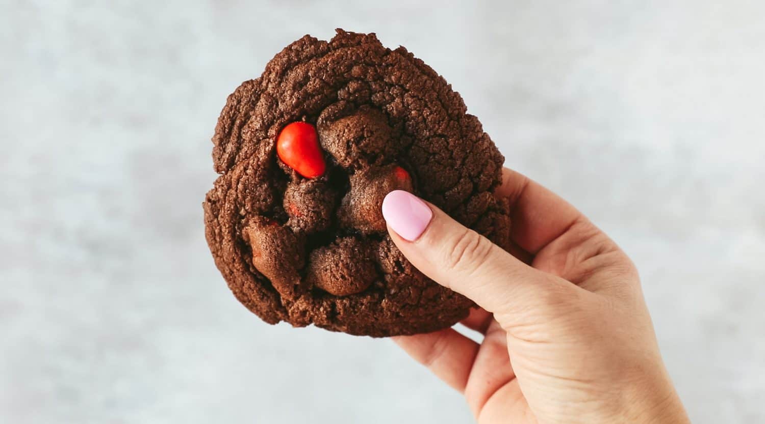 A hand holding a huge chocolate mini egg cookie.