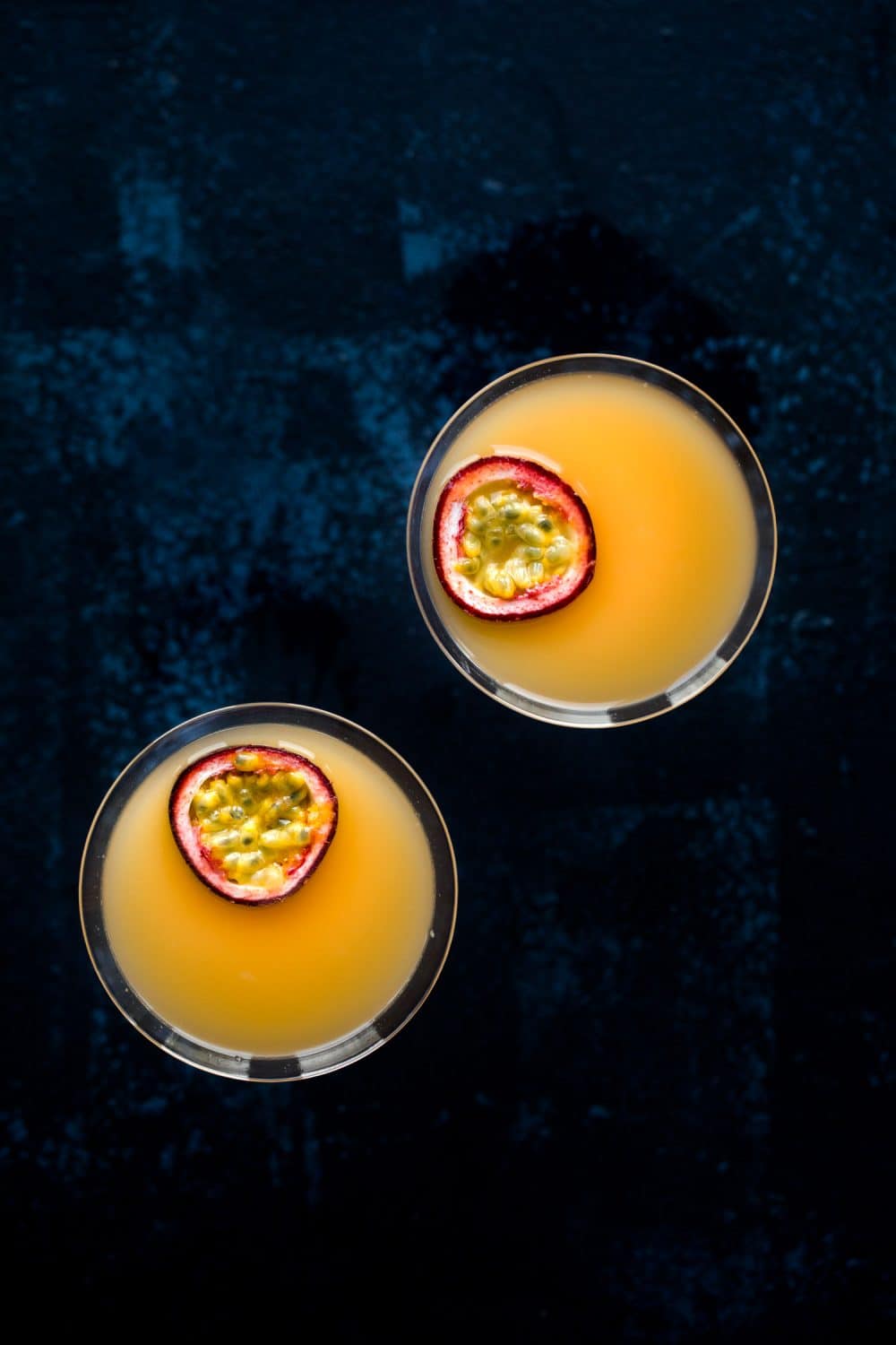 Overhead view of two pornstar martini cocktails with passion fruit slices floating on top. 