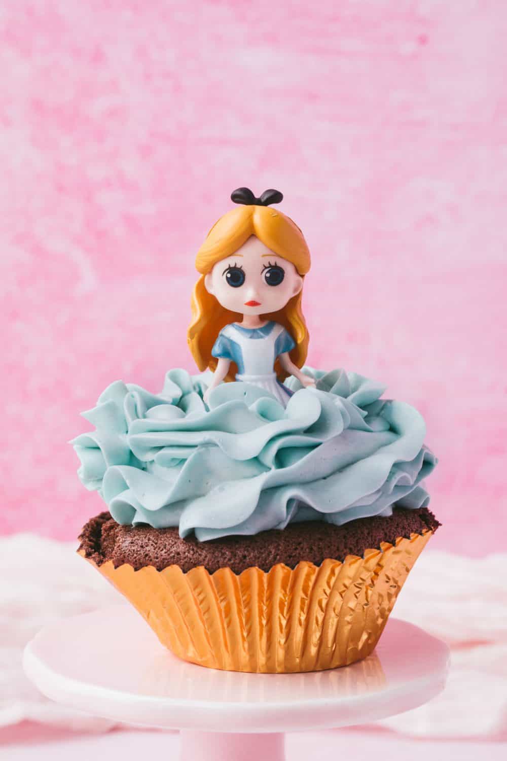 Alice in Wonderland cupcake topper on a chocolate cupcake with blue buttercream frosting. 