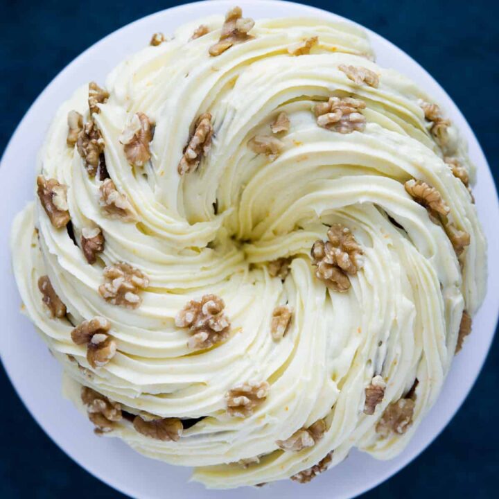 A carrot cake bundt that has been covered in a cream cheese frosting with walnuts.