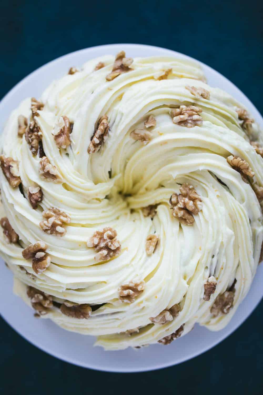 A carrot cake bundt cake covered in cream cheese frosting and walnuts. 