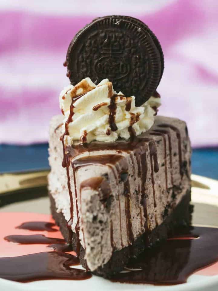 A slice of Oreo Cheesecake that has been drizzled with chocolate sauce.