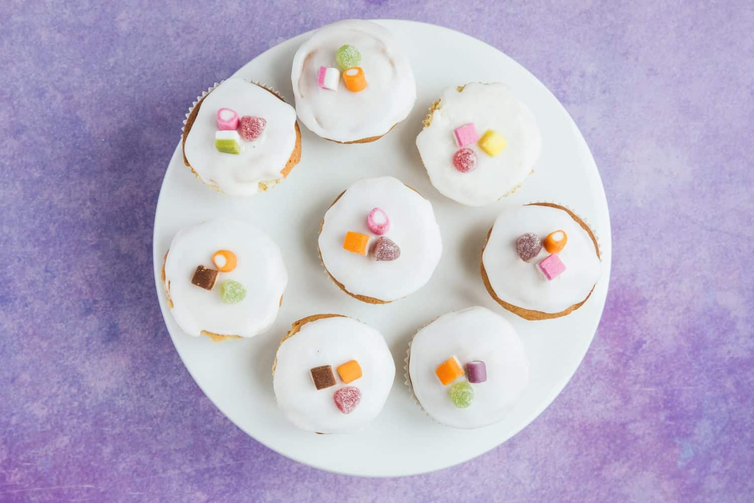 A white cake stand with 8 fairy cakes on top. 