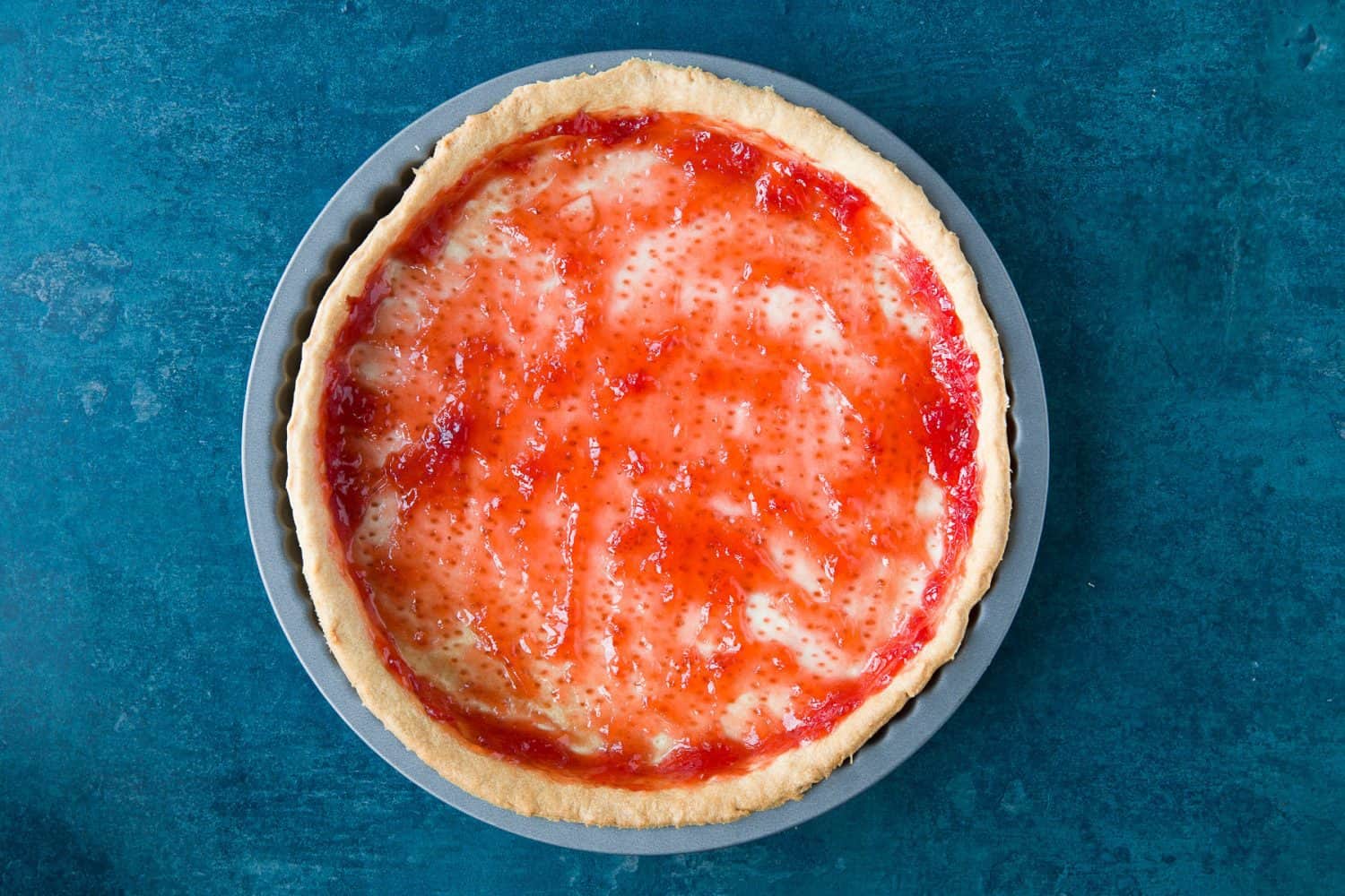 Strawberry jam spread over the top of cooked shortcrust pastry. 