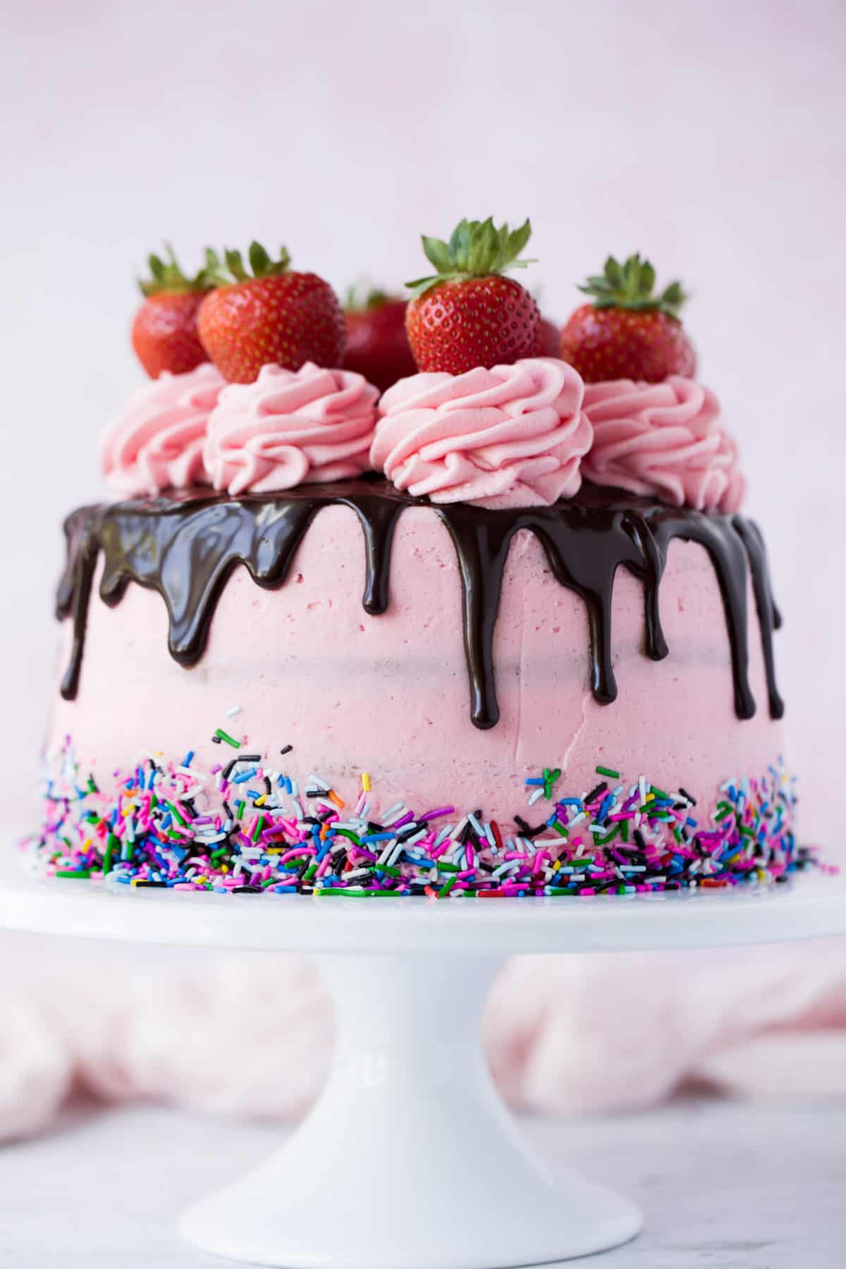 A pink cake with a chocolate drip and strawberries on the top. 