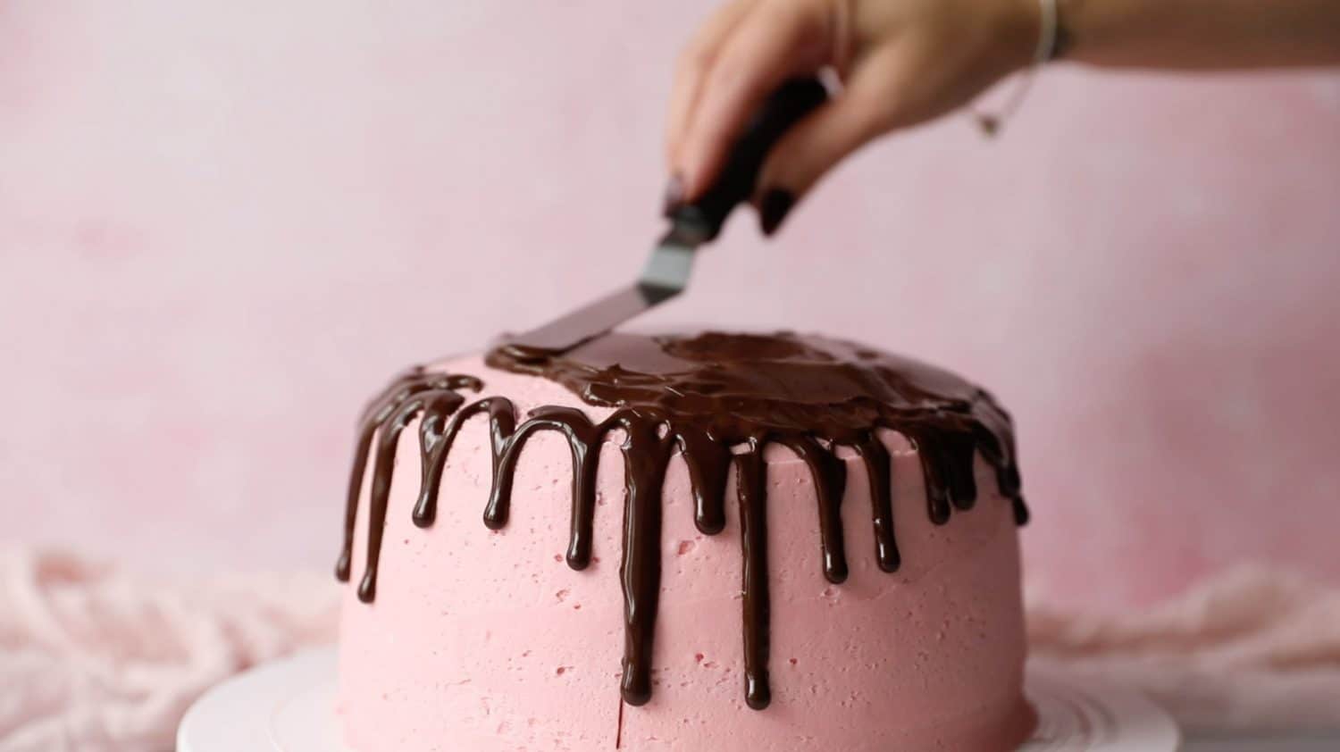 A palette knife smoothing chocolate ganache over the top of a cake. 