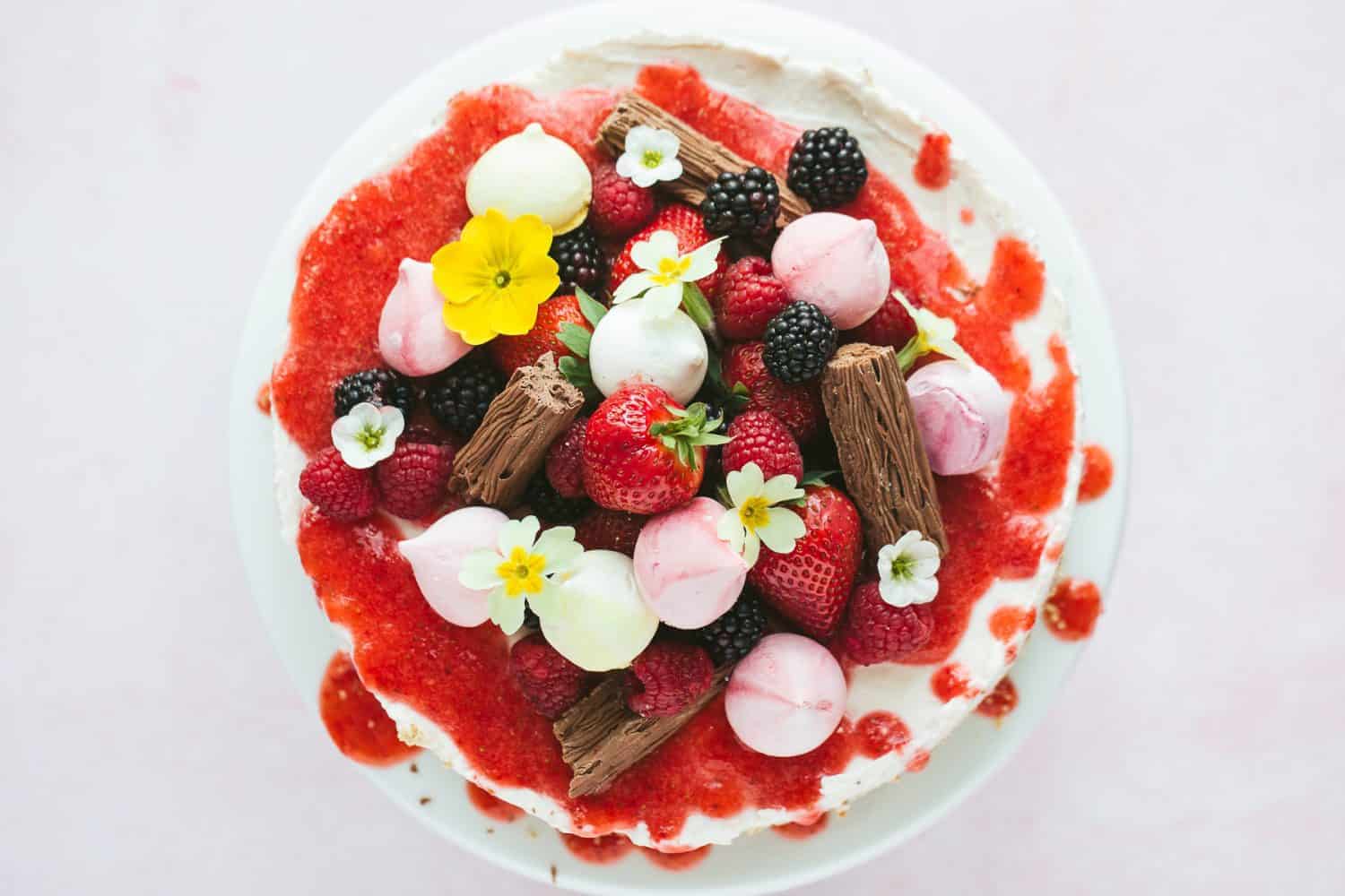 mini meringues, strawberries, blackberries, raspberries and chocolate flakes on top of a cheesecake. 