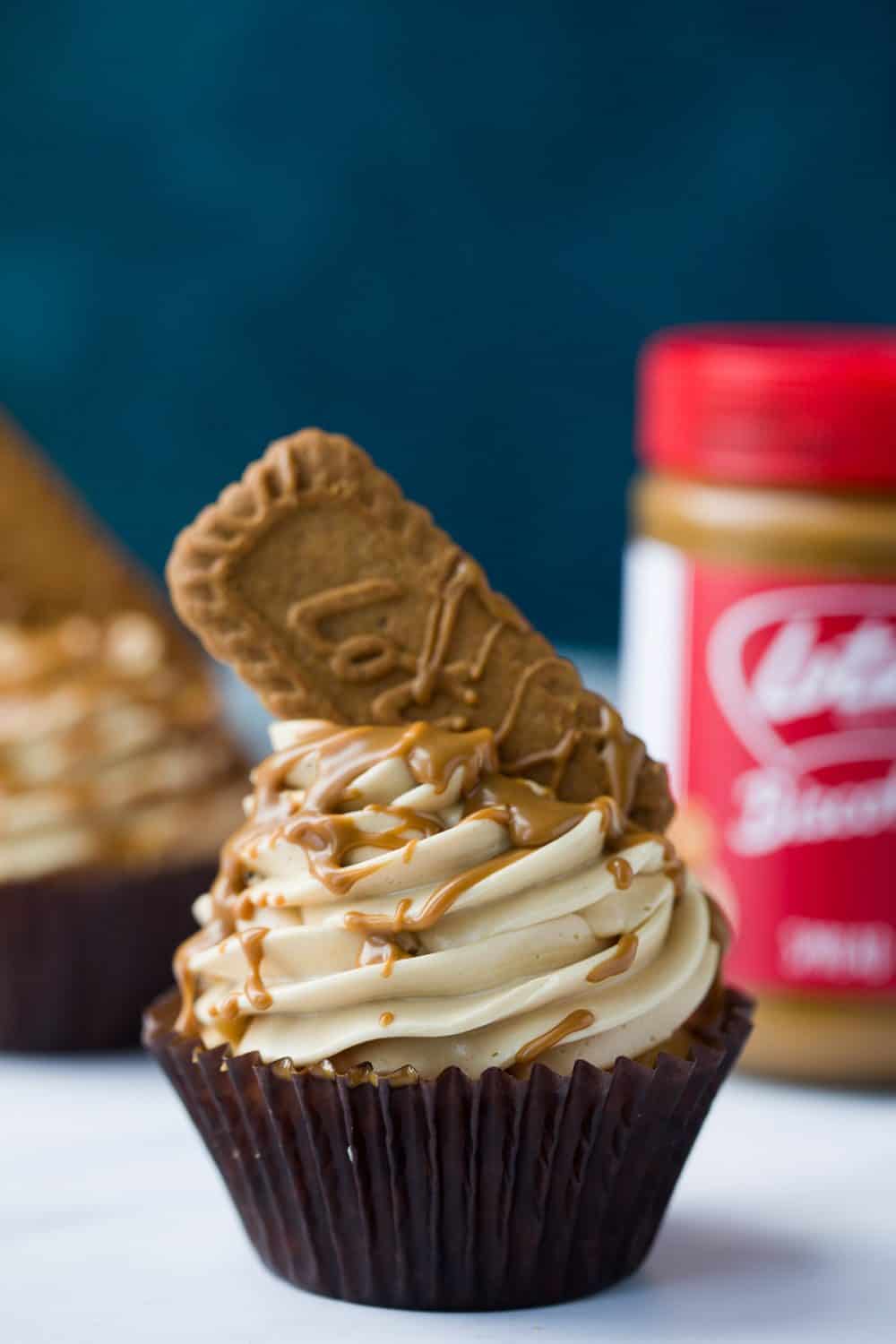 A Lotus Biscoff Cupcake with a red jar of Biscoff spread in the background. 