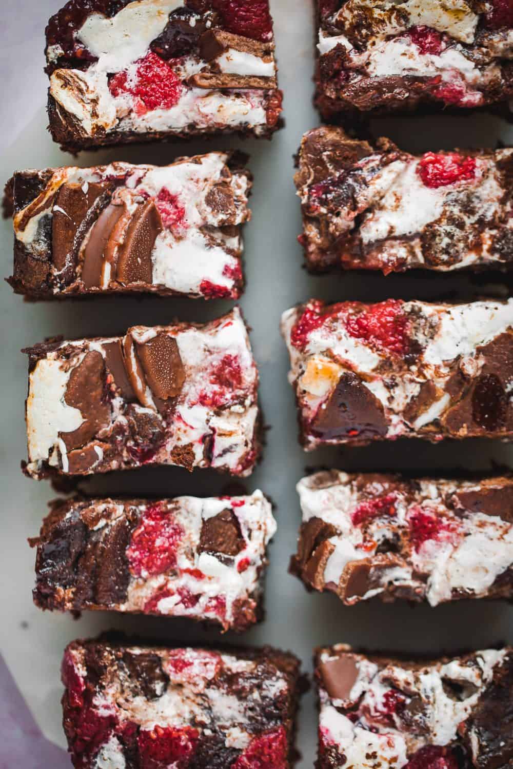 Slices of chocolate brownies topped with marshmallow, raspberries and wagon wheels. 