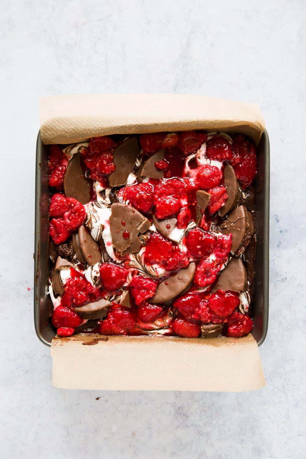 A tin of chocolate brownie batter topped with marshmallow fluff, wagon wheels and raspberries. 