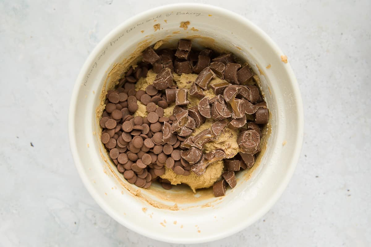 A mixing bowl with cookie dough, chocolate chips and chopped up rolos. 