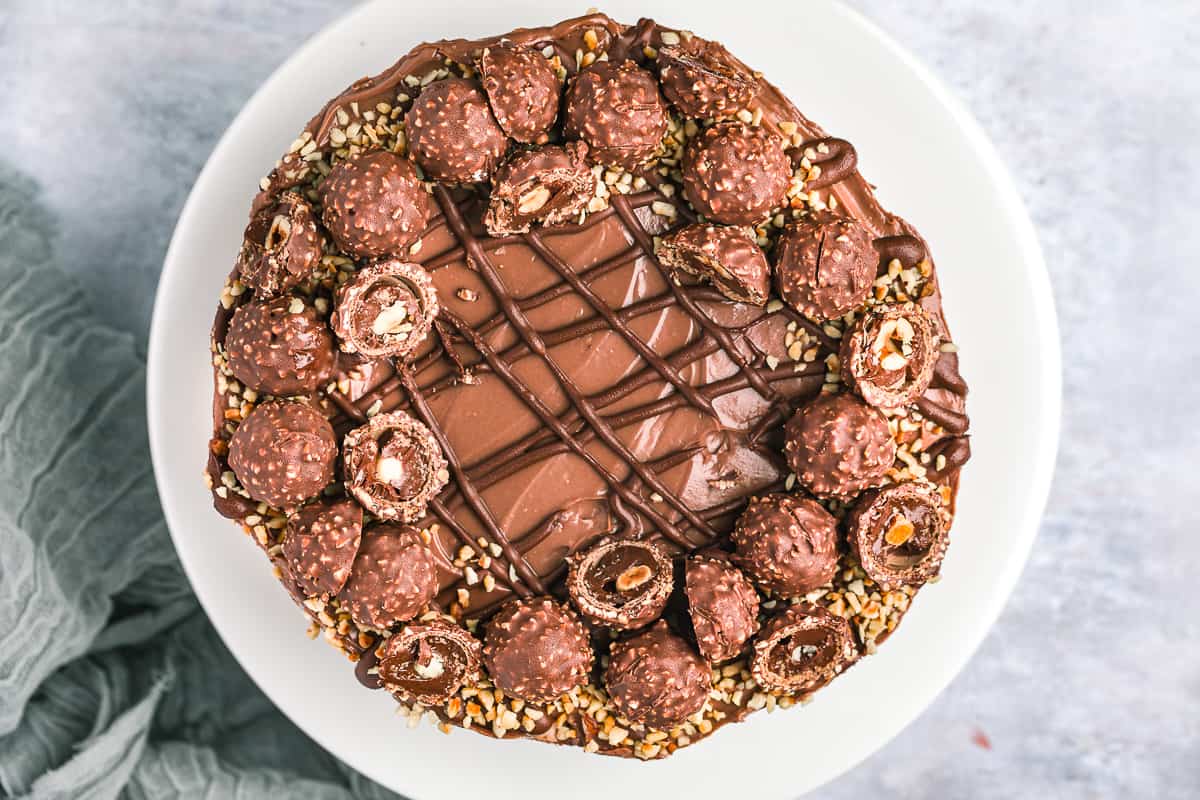 A no bake cheesecake decorated with drizzled Nutella, chopped hazelnuts and Ferrero Rocher.