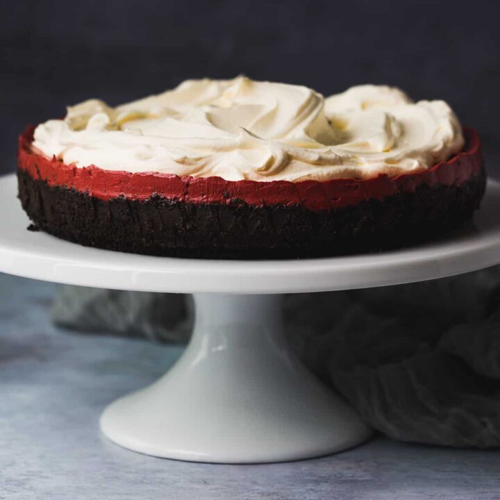 A red velvet cheesecake on a white cake stand