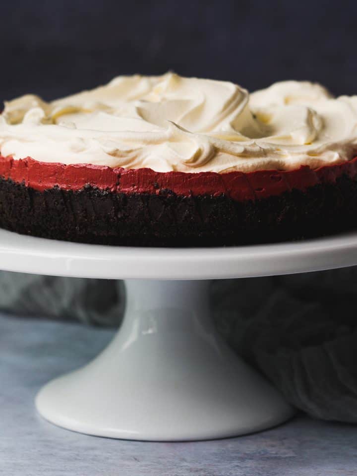 A red velvet cheesecake on a white cake stand