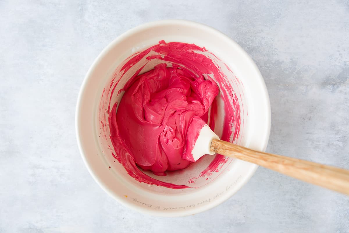 A mixing bowl with a cream cheese and double cream mixture that has been coloured with red food colouring. 