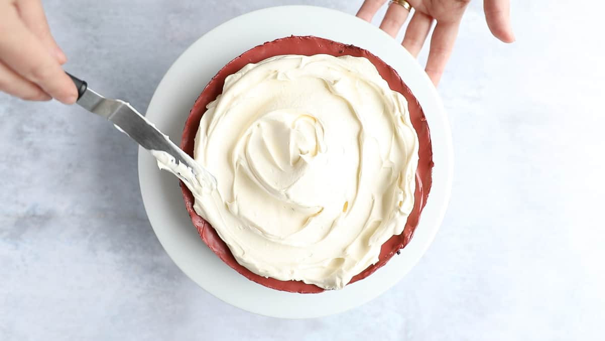 Using an off set spatula to spread whipped cream on top of cheesecake filling. 