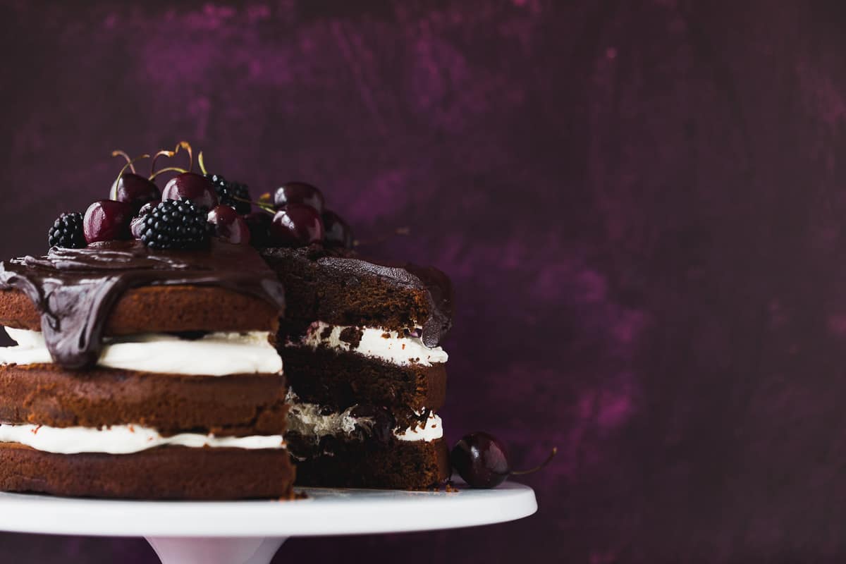 A black forest gateau that has a slice cut out of it. There are cherries and blackberries on top. 