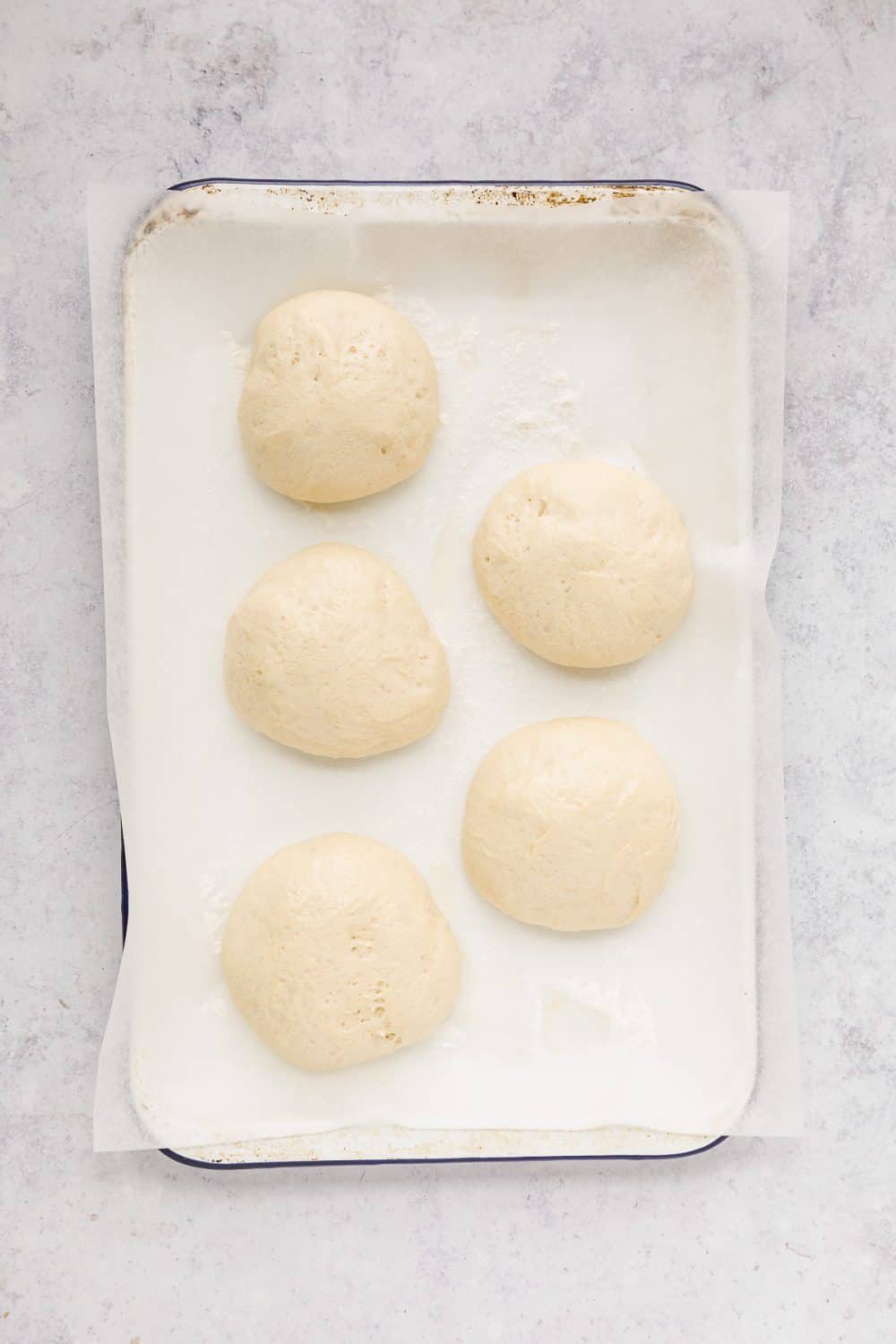 5 risen balls of doughnut dough on a white baking tray lined with baking paper. 