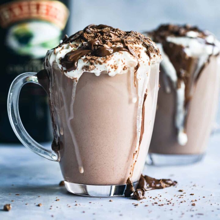 Baileys Hot Chocolate in a glass mug with cream on top, a flake crumbled over and chocolate sauce.