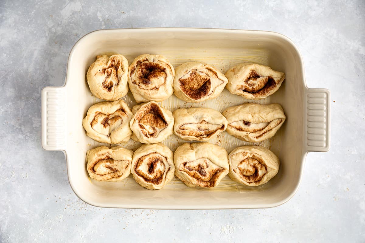 A rectangular white baking dish that contains 12 unbaked Cinnamon Buns. 