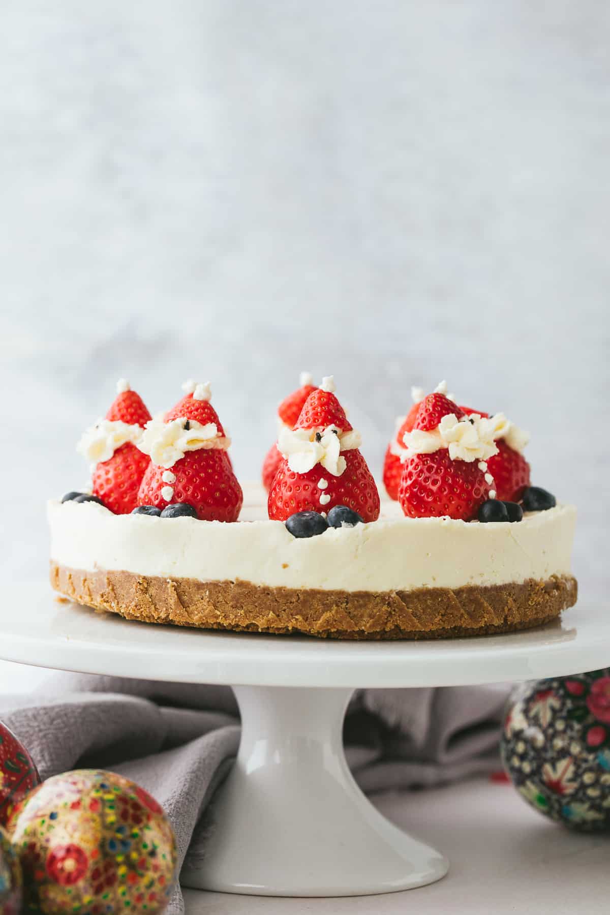 A white chocolate cheesecake with a gingernut biscuit base. There are strawberries on top of the cheesecake that have been made to look like Santas. 