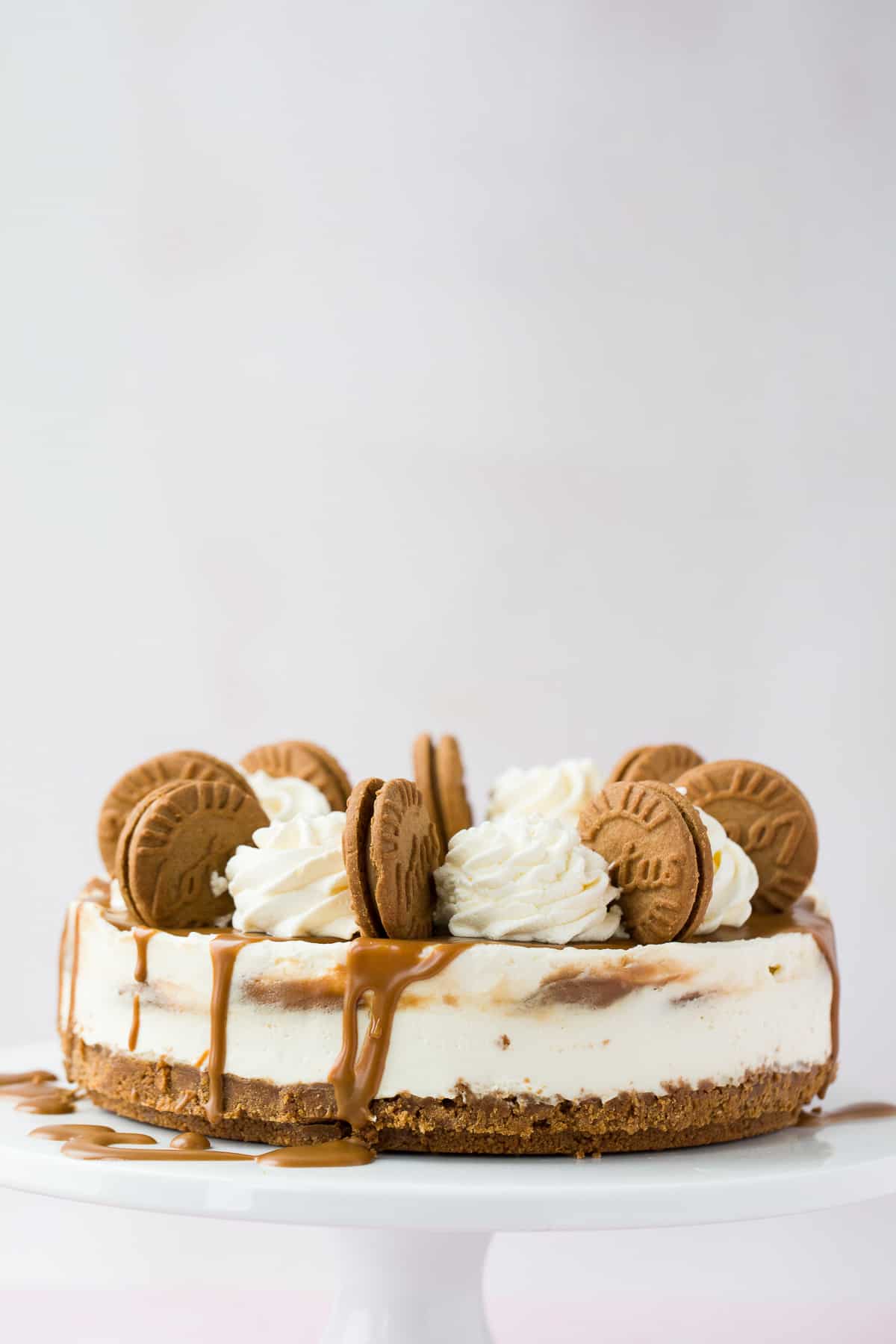 A biscoff flavoured cheesecake on a white cake stand. 