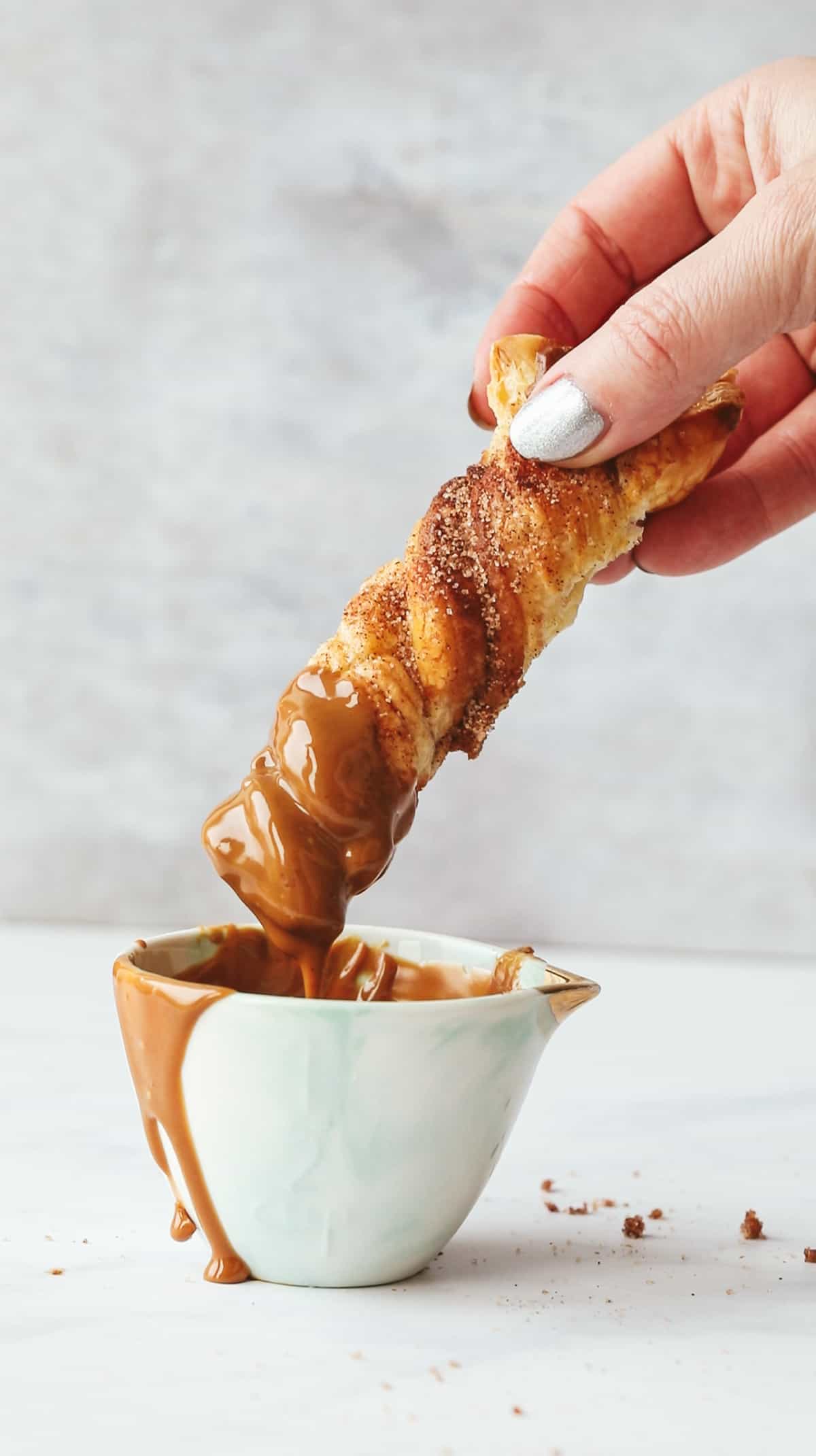 Holding a churro stick and dipping it into warm biscoff spread. 
