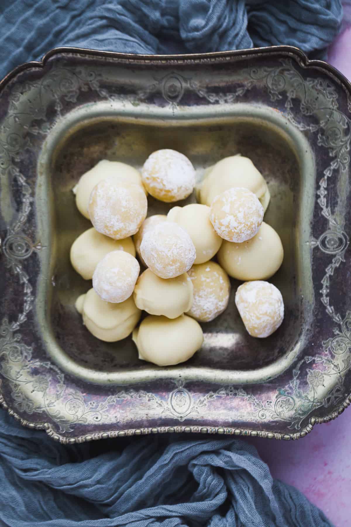 A vintage tray filled with white chocolate and lemon truffles. Half of them have been coated in icing sugar while the other half have been coated in white chocolate. 