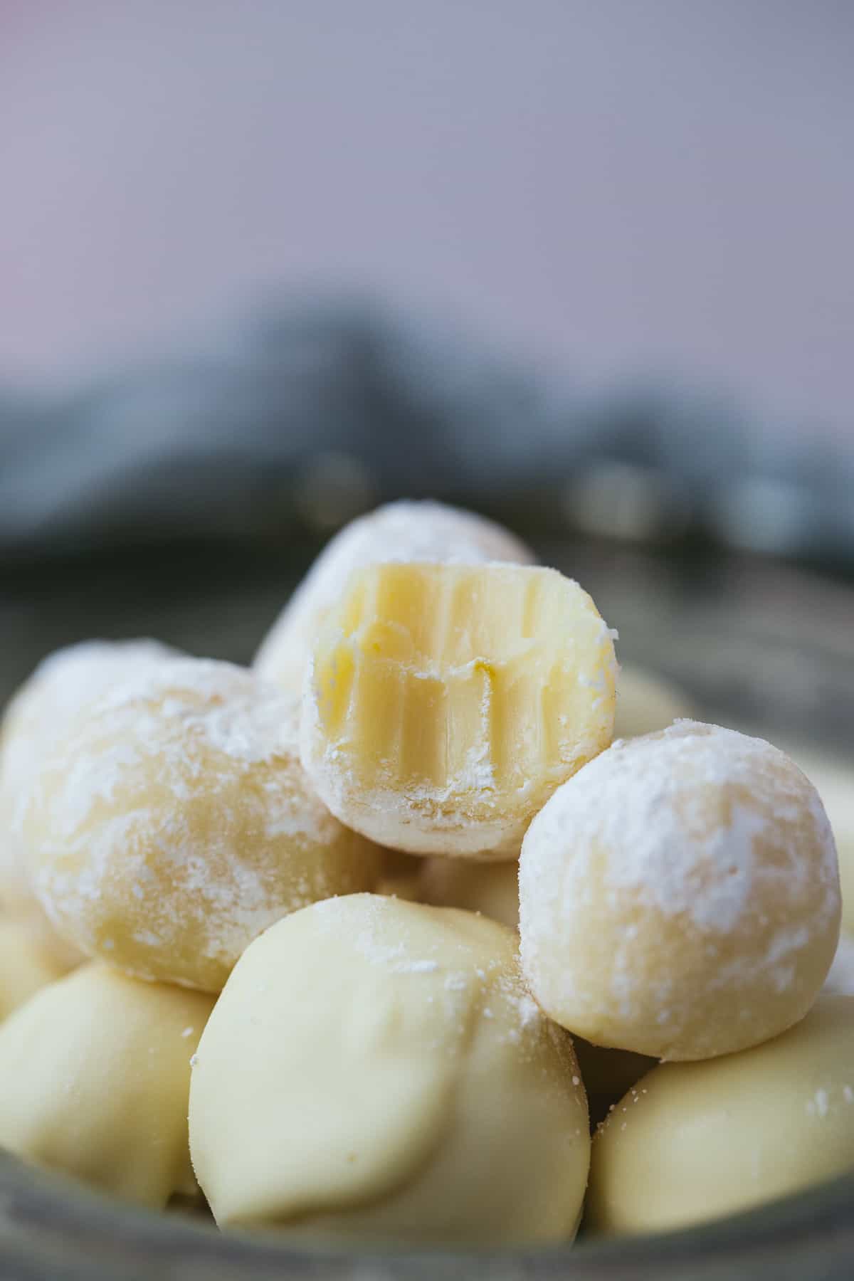 Close up image of a pile of white chocolate and lemon truffles. The truffle on top of the pile has had a bite taken out of it and teeth marks are visible. 