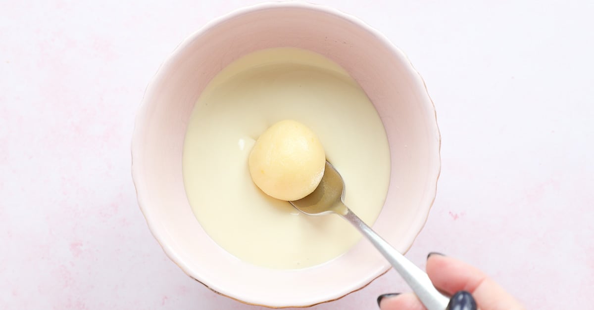 A truffle on top of a fork being lowered into melted white chocolate. 
