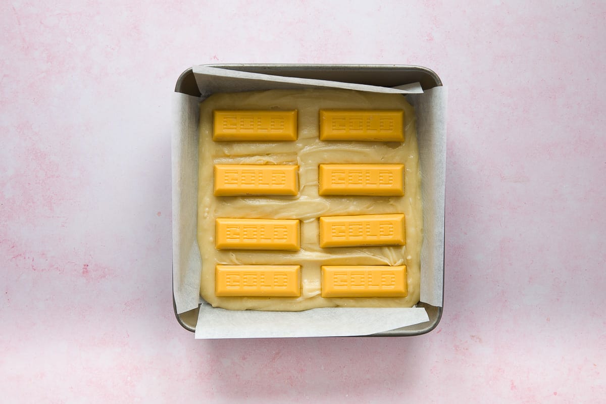 A square baking tin containing blondie mixture and 8 Mcvities Gold bars. 