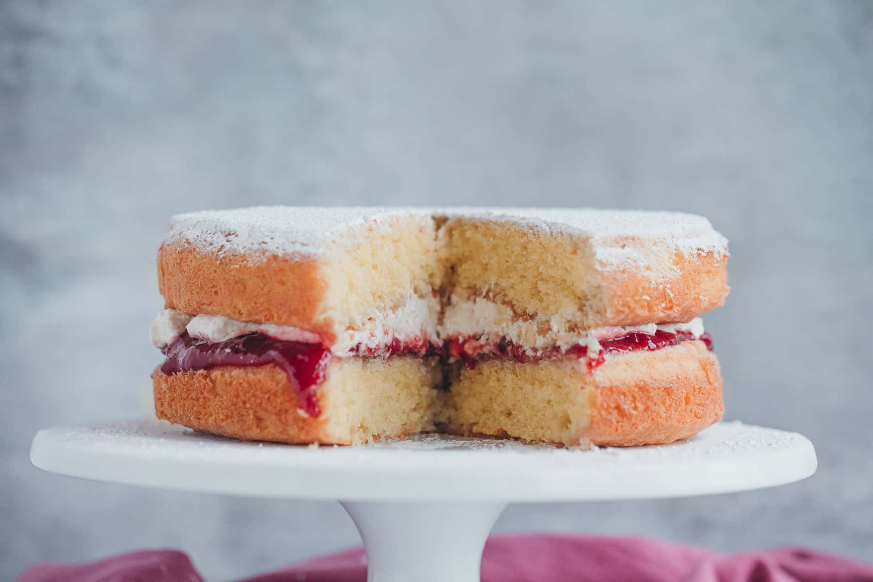 A Victoria Sandwich cake that has been sliced open. There is a cream and jam filling. 