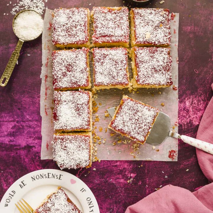Squares of jam and coconut sponge cake on a pink background.