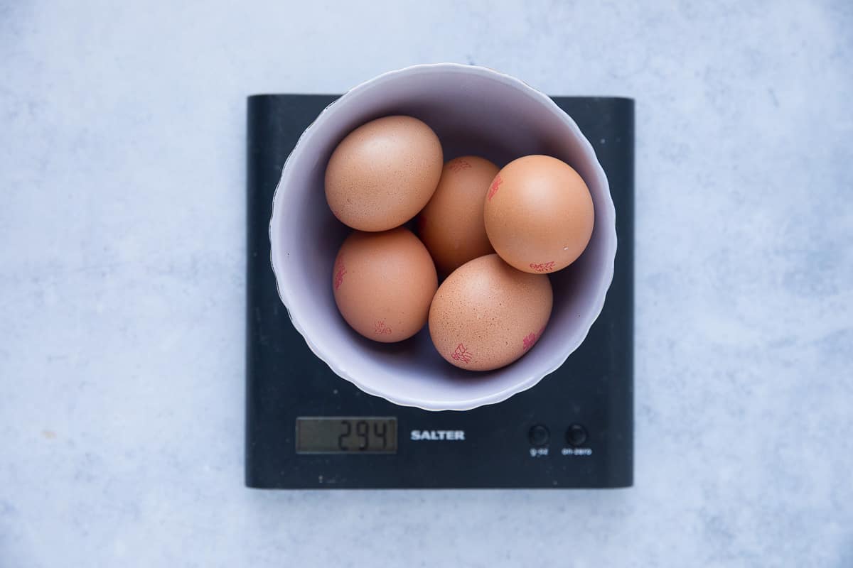 5 eggs in their shells inside a bowl that has been put onto a weighing scale. 