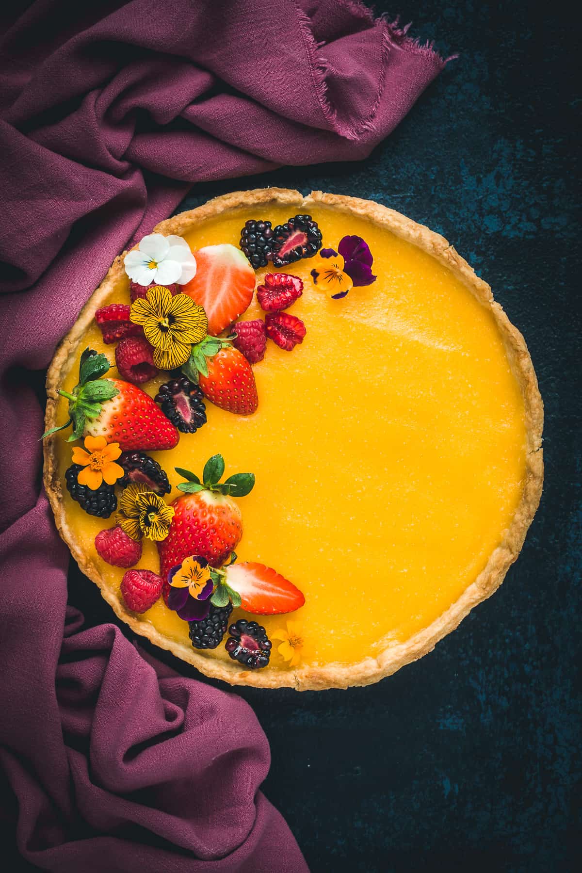 A French Lemon Tart decorated with fresh berries and edible flowers. 