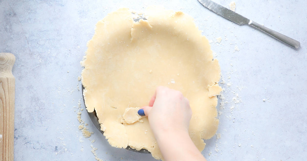 Using spare pastry to repair the tears in a shortcrust pastry base. 