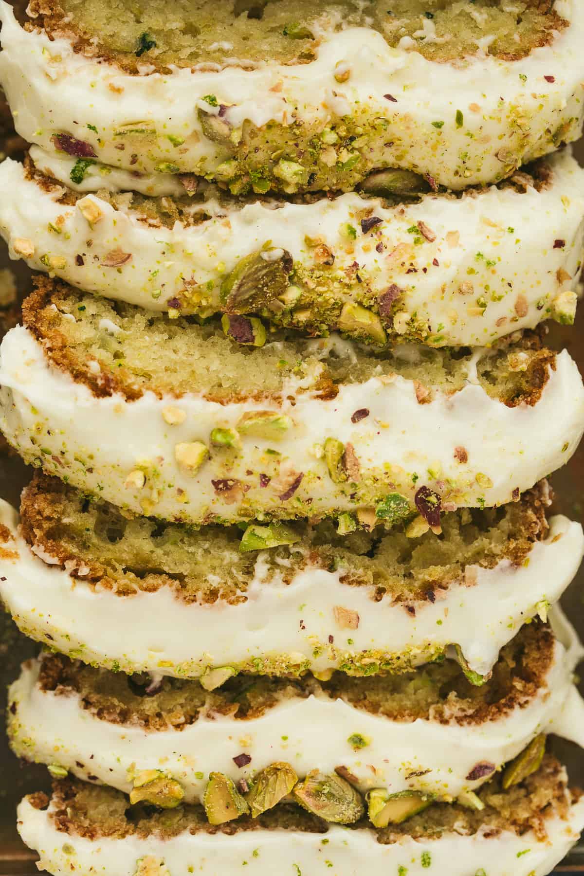 A zucchini cake cut into slices and topped with frosting and chopped pistachios. 