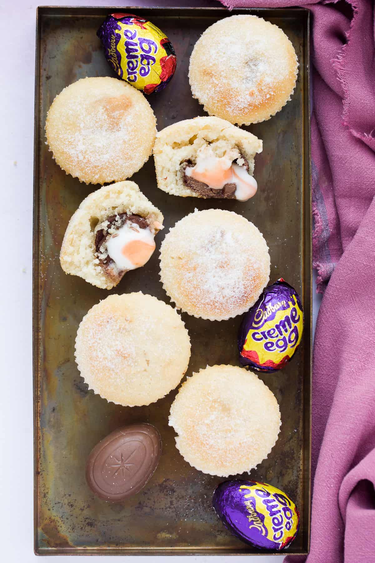 Doughnut muffins with creme eggs on a baking tray. 