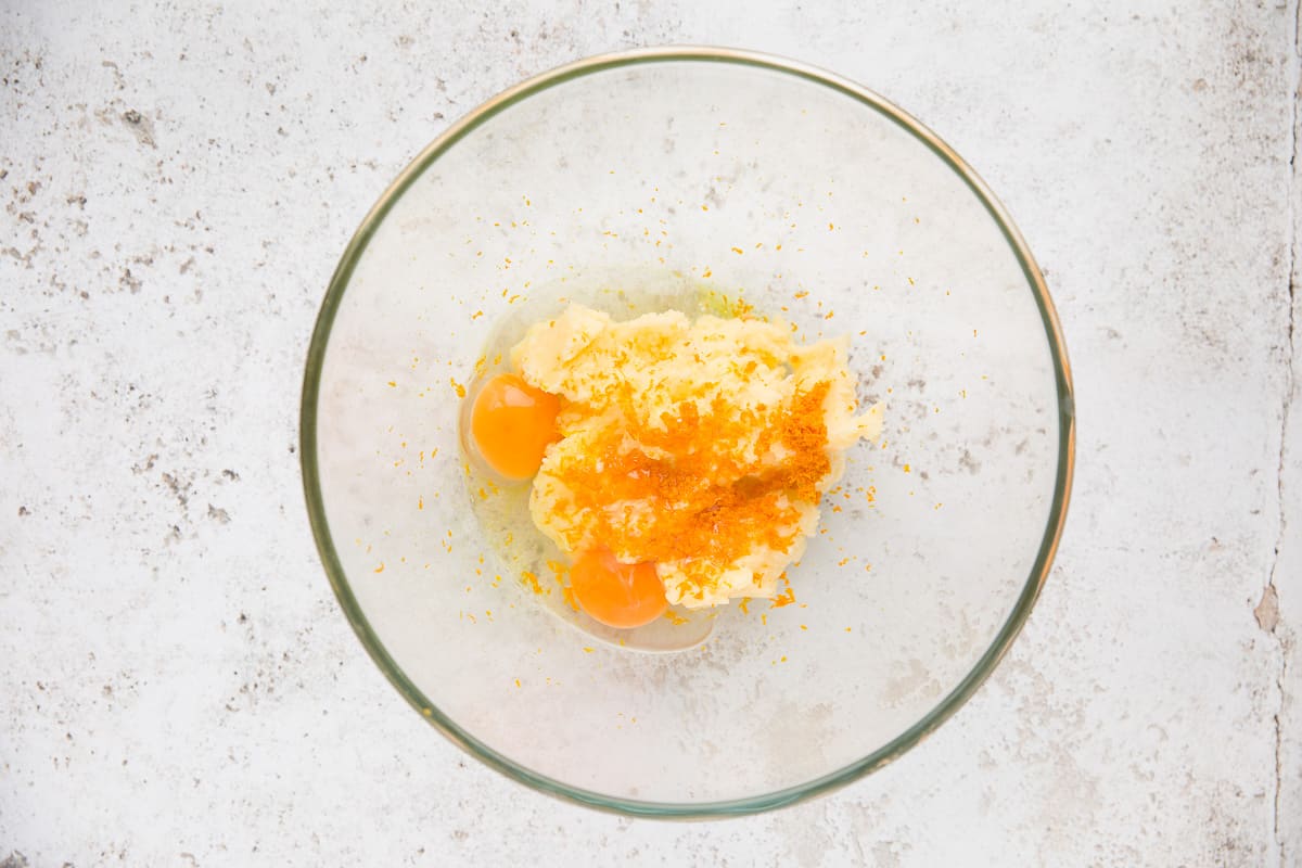 A glass mixing bowl that has had eggs and orange zest added to the creamed mixture. 