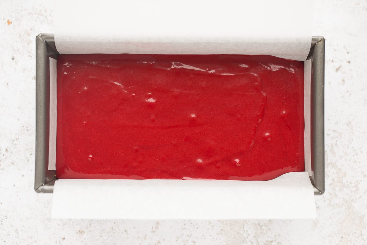 A 2lb loaf pan has been filled with red coloured cake mixture. 