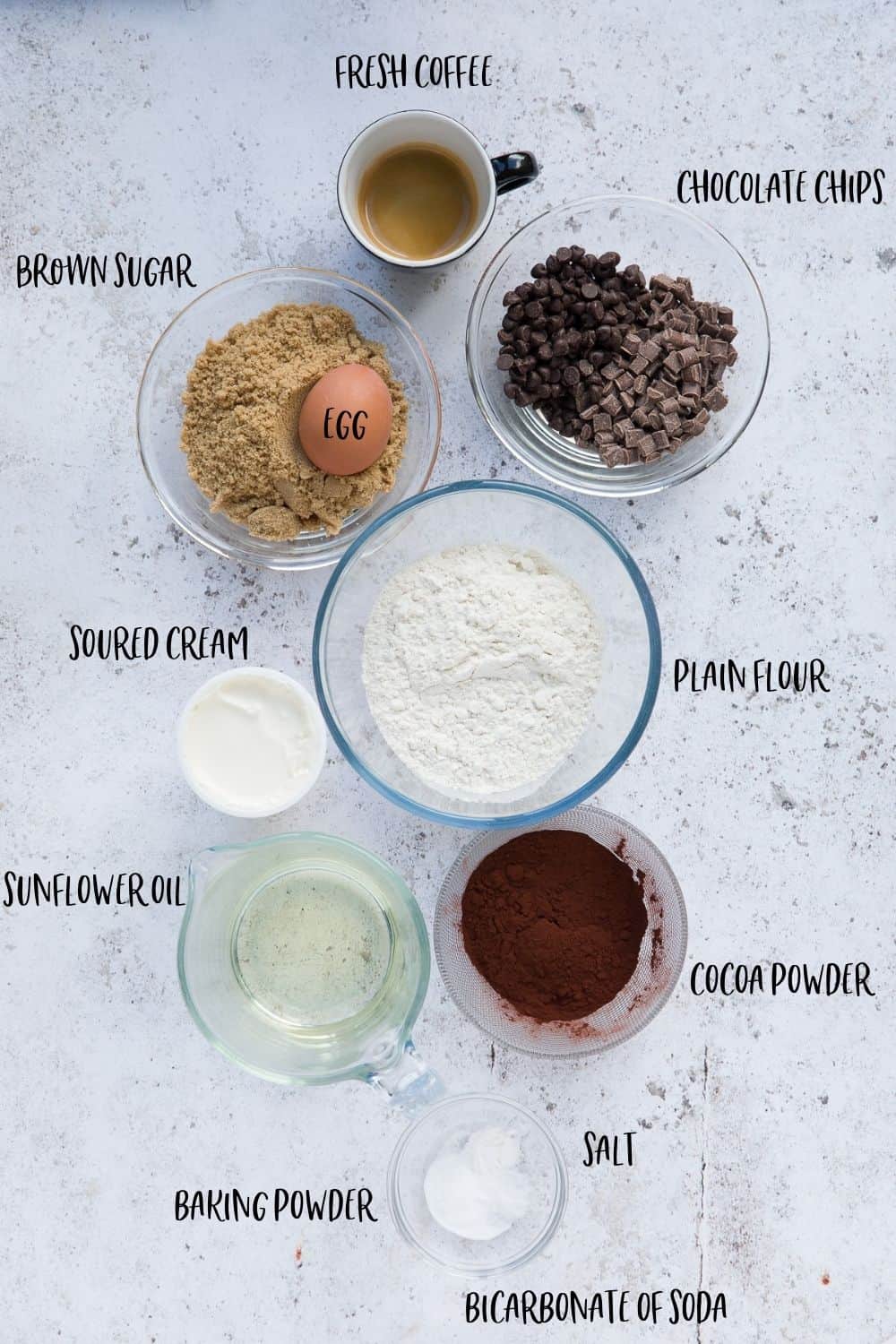 An image showing the following ingredients in glass bowls: fresh coffee, chocolate chips, brown sugar, egg, plain flour, soured cream, sunflower oil, cocoa powder, baking powder, salt and bicarbonate of soda. 