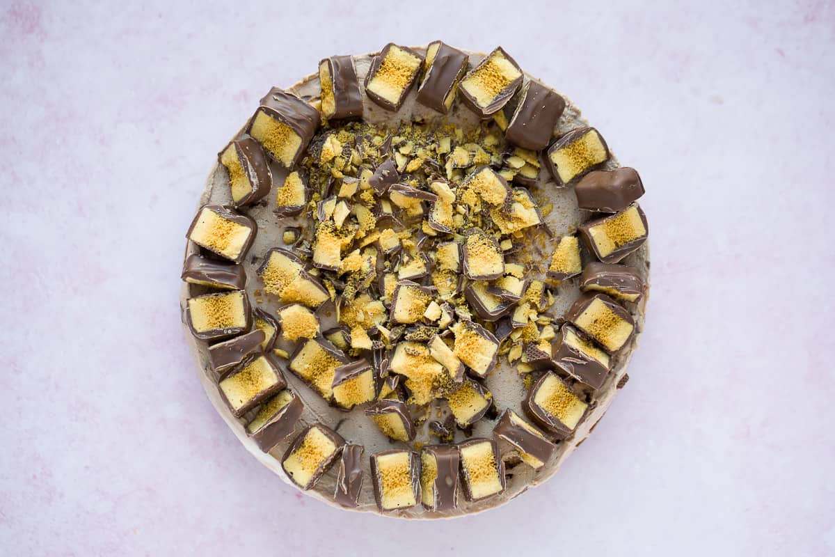 Overhead image of a round cheesecake that has been covered in crushed Crunchie bars. 