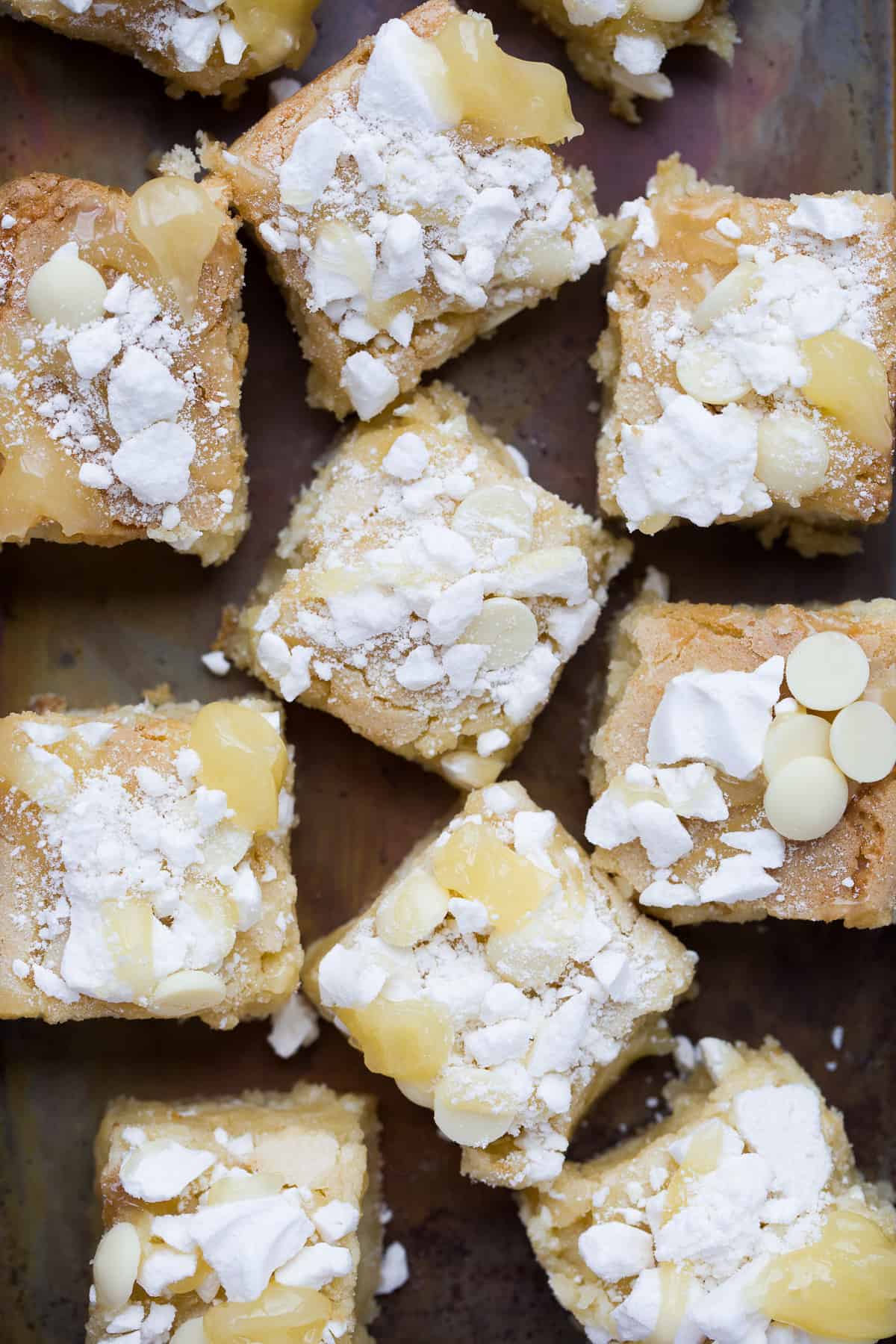 Squares of lemon meringue blondies on a dark coloured baking tray. 