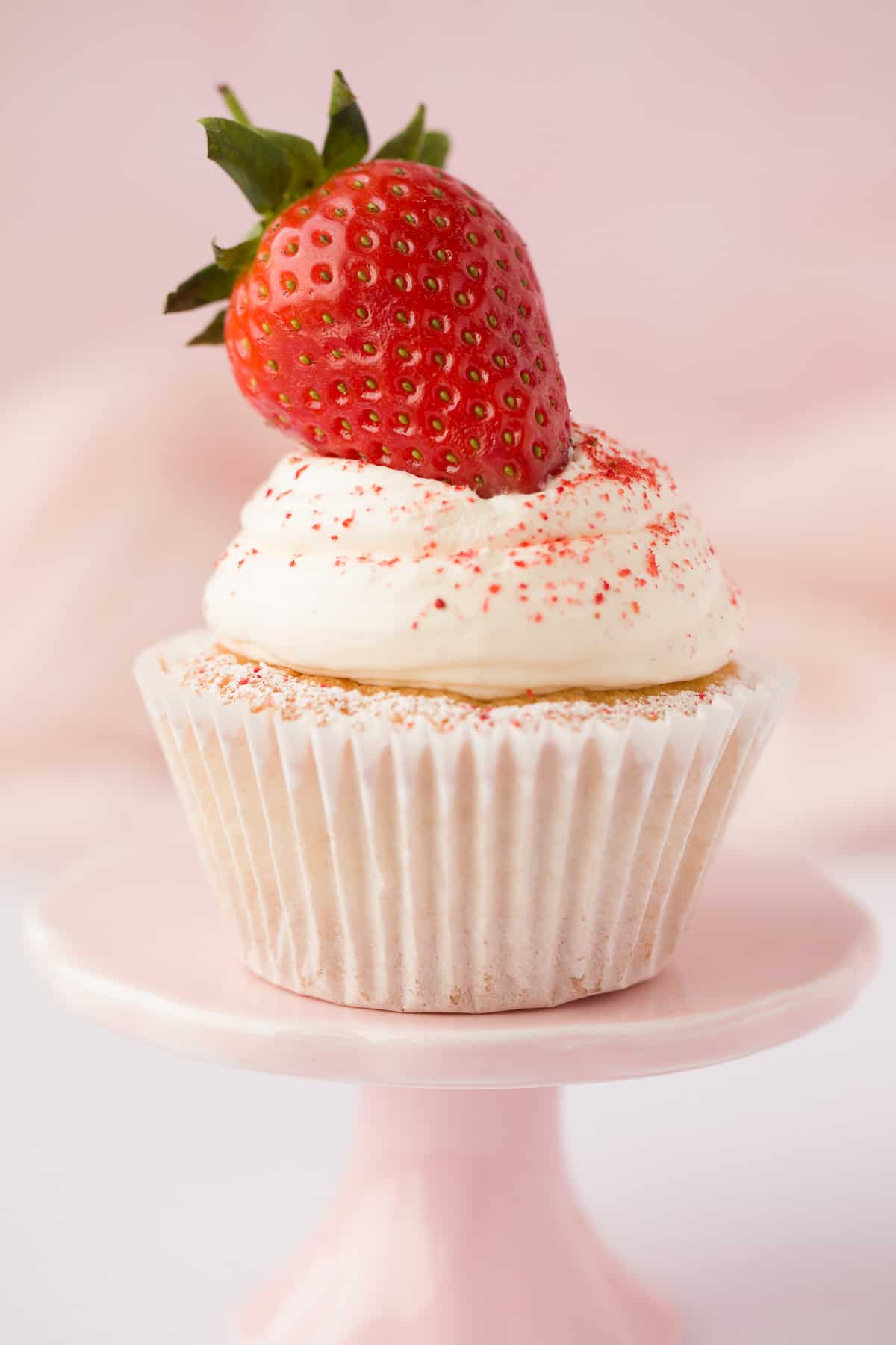 A Victoria Sponge Cupcake with a whipped cream topping and strawberry decoration. 