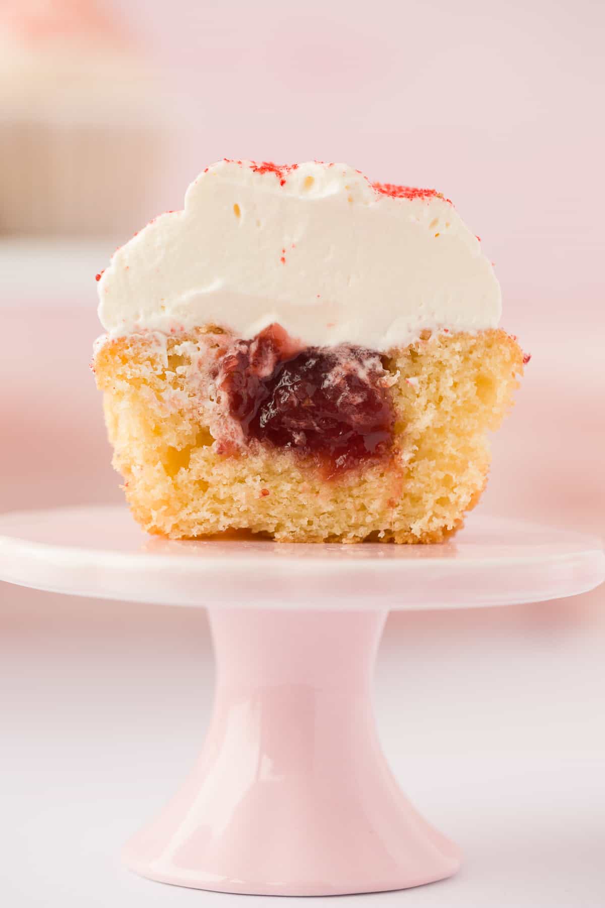A Victoria Sponge Cupcake that has been cut open to reveal the strawberry jam filling. 