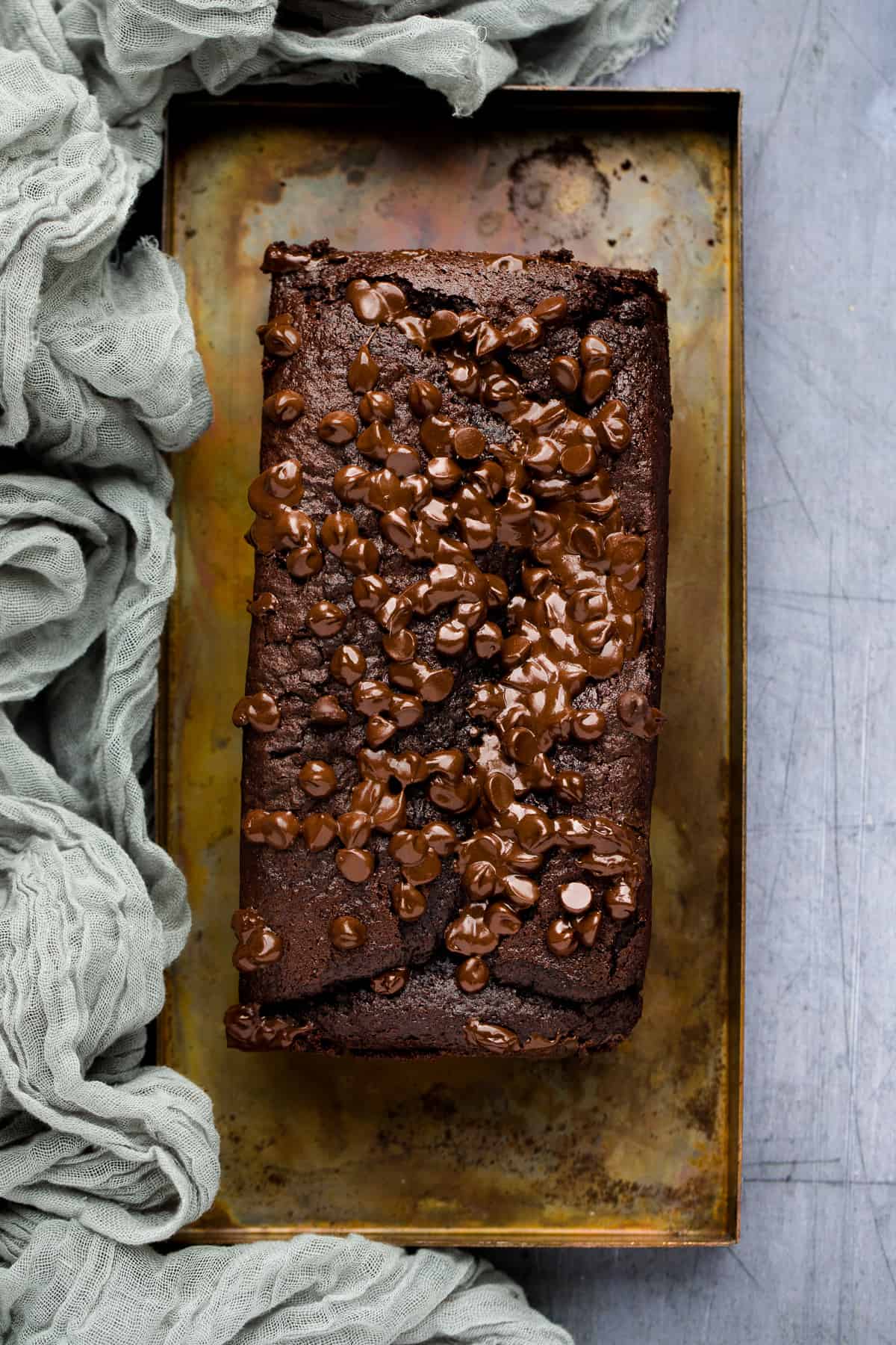 A perfect chocolate loaf cake on a metal tray with a green cloth next to it. 