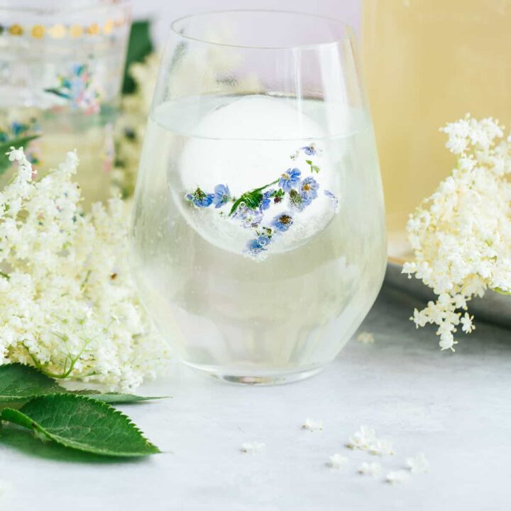 A glass of Elderflower cordial surrounded by flowers.